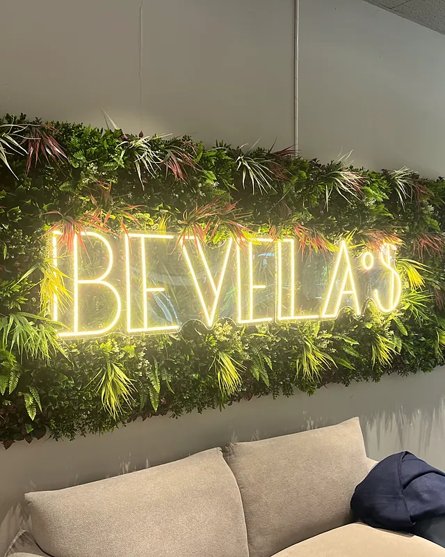 Der Neon-Schriftzug Bevela's auf der Pflanzenwand, schräg von der Seite fotografiert